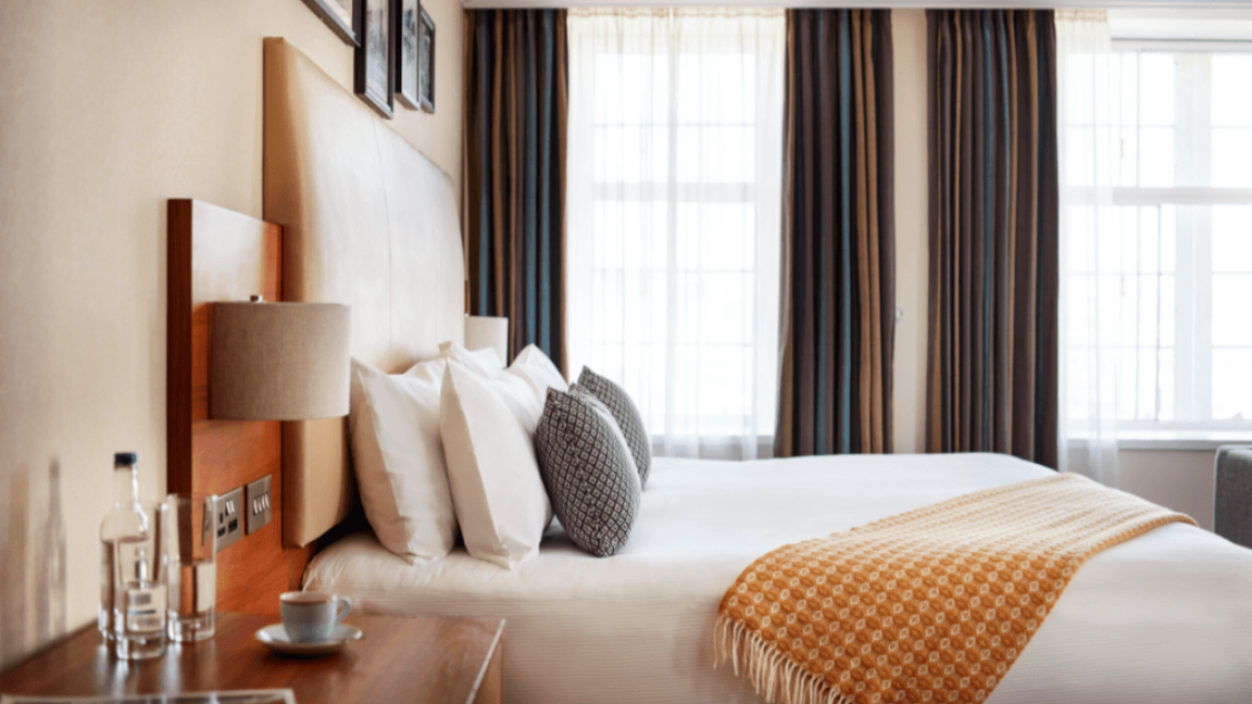 Comfortable hotel room with a double bed, bedside table and natural light, highlighting overnight accommodation for business travellers.